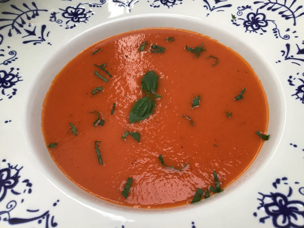 Primer plano de la crema o sopa de tomate servida en un plato de loza con decoración fina. 
