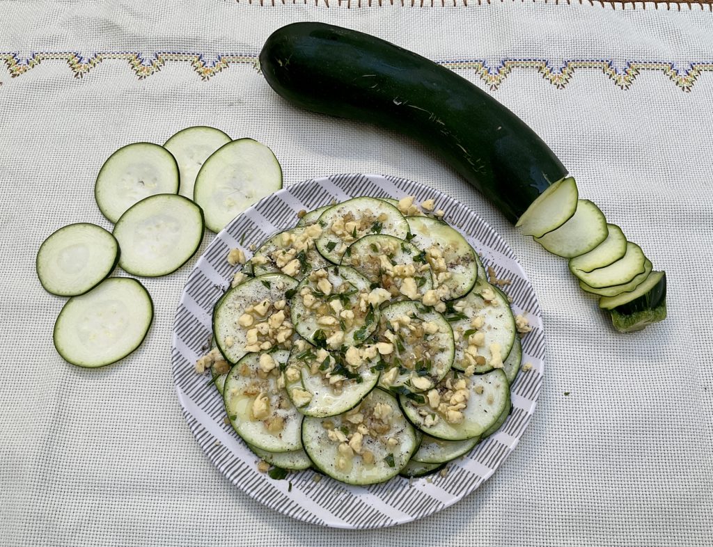 Plato decorado. Carpaccio de calabacín y nueces servido y decorado con perifollo fresco picado. Al lado del plato un calabacín a medio lonchear.