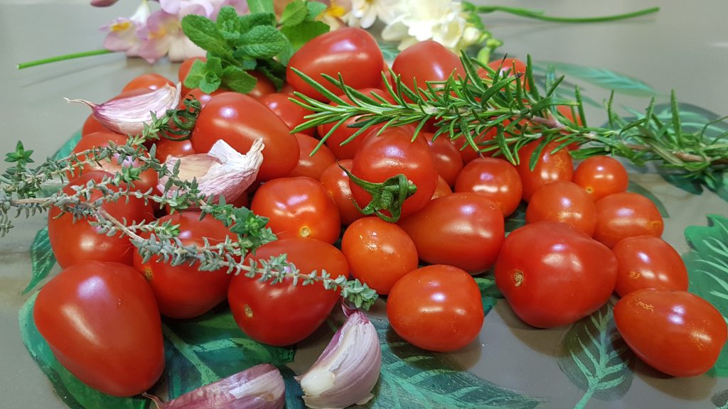 Bodegón formado por tomatitos Cherry, unos ajos y varias aromáticas.
